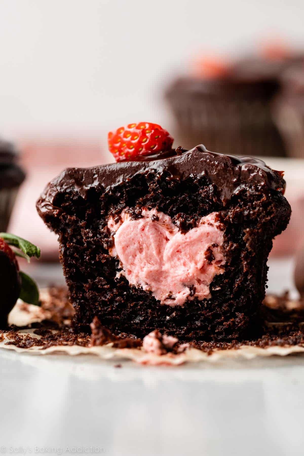 close-up of chocolate cupcake topped with chocolate ganache and filled with strawberry buttercream.