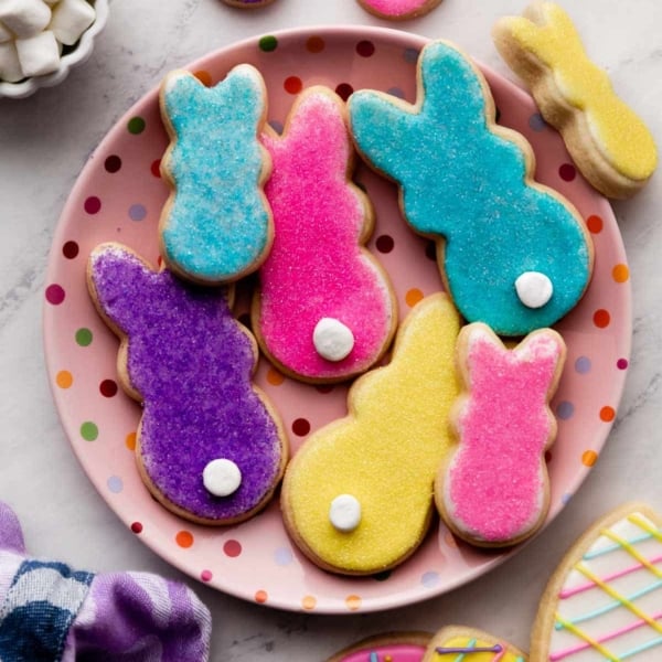 PEEPS marshmallow-inspired bunny sugar cookies with marshmallow tails on pink polka dot plate with Easter egg decorated sugar cookies in bottom corner.