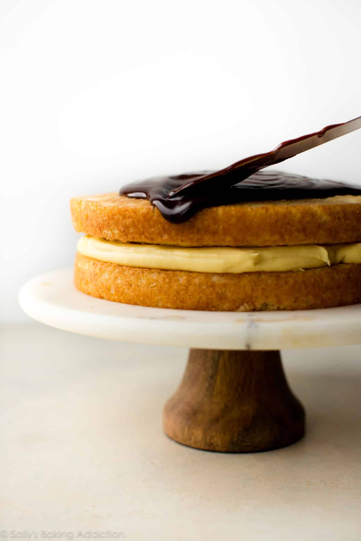 spreading chocolate ganache topping onto Boston cream pie