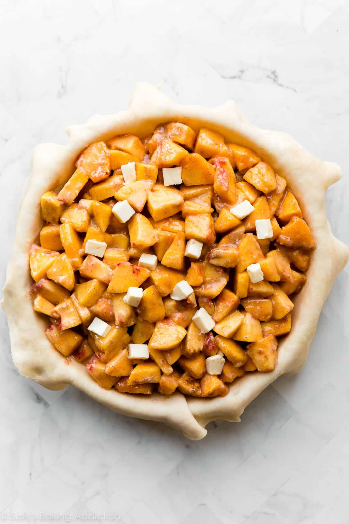 peaches in pie crust with cubes of butter dotted on top.