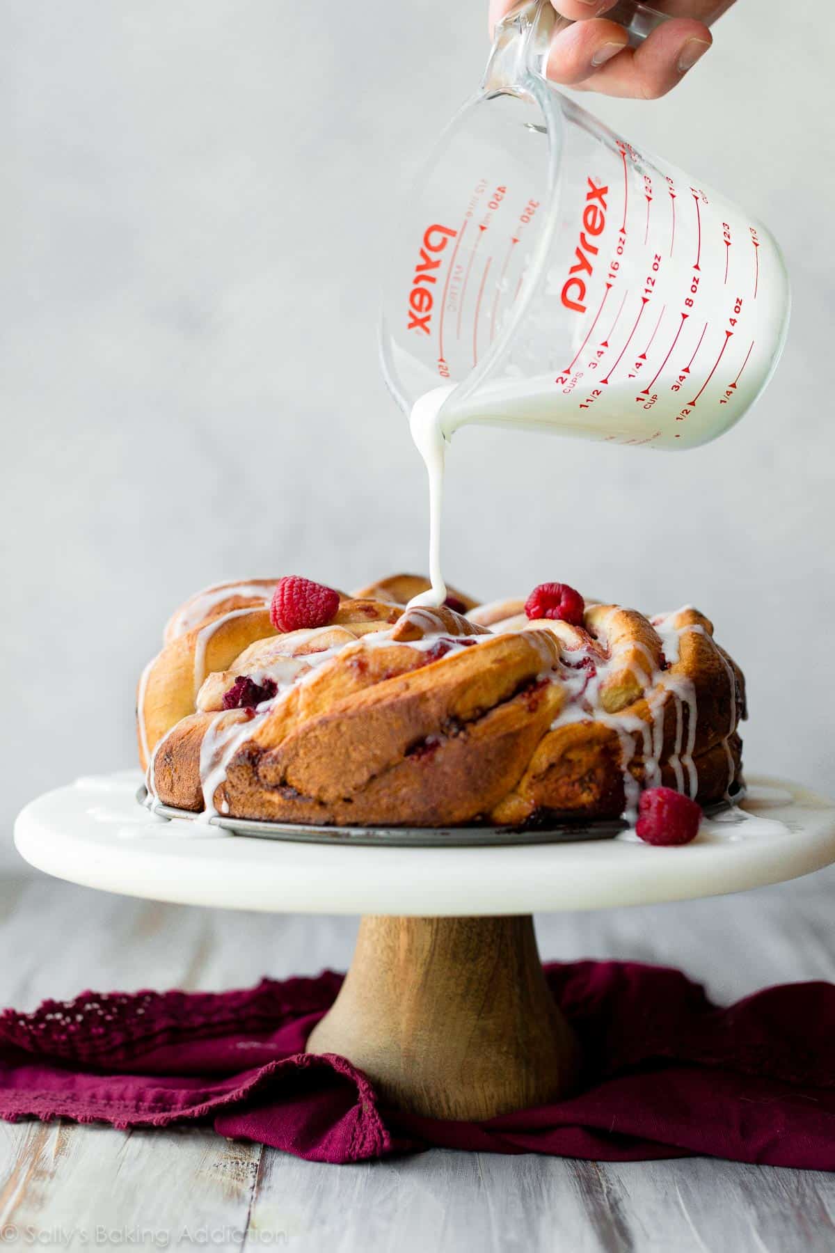 Pouring vanilla icing on top of raspberry danish twist