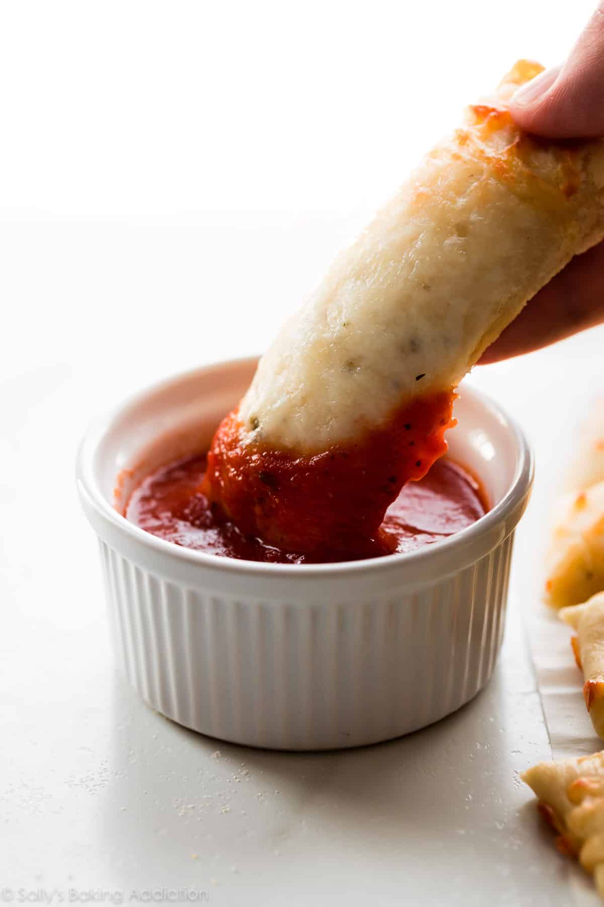 dipping cheese breadsticks into bowl of marinara sauce