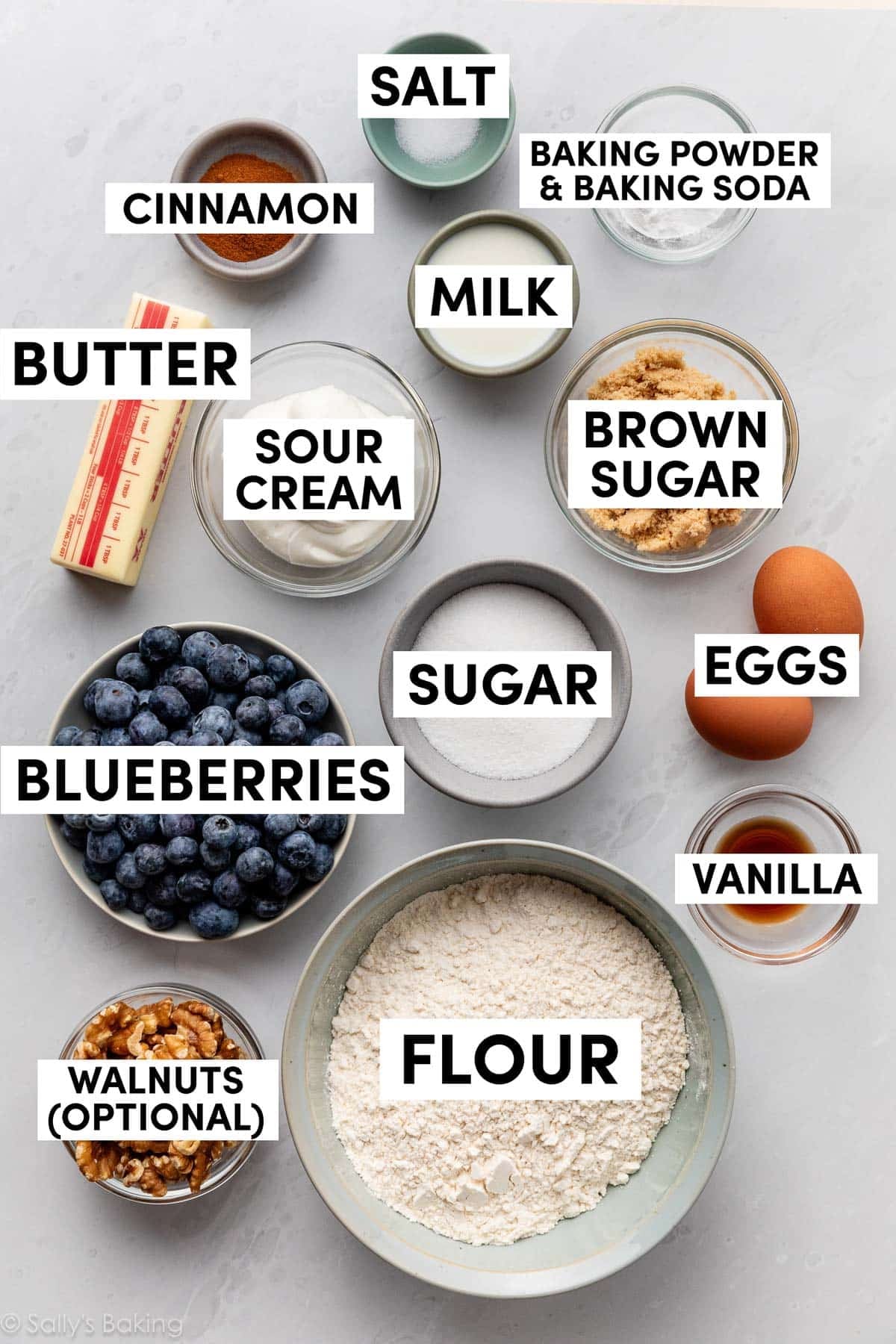 ingredients on marble surface including flour, sugar, eggs, vanilla, butter, cinnamon, and milk.