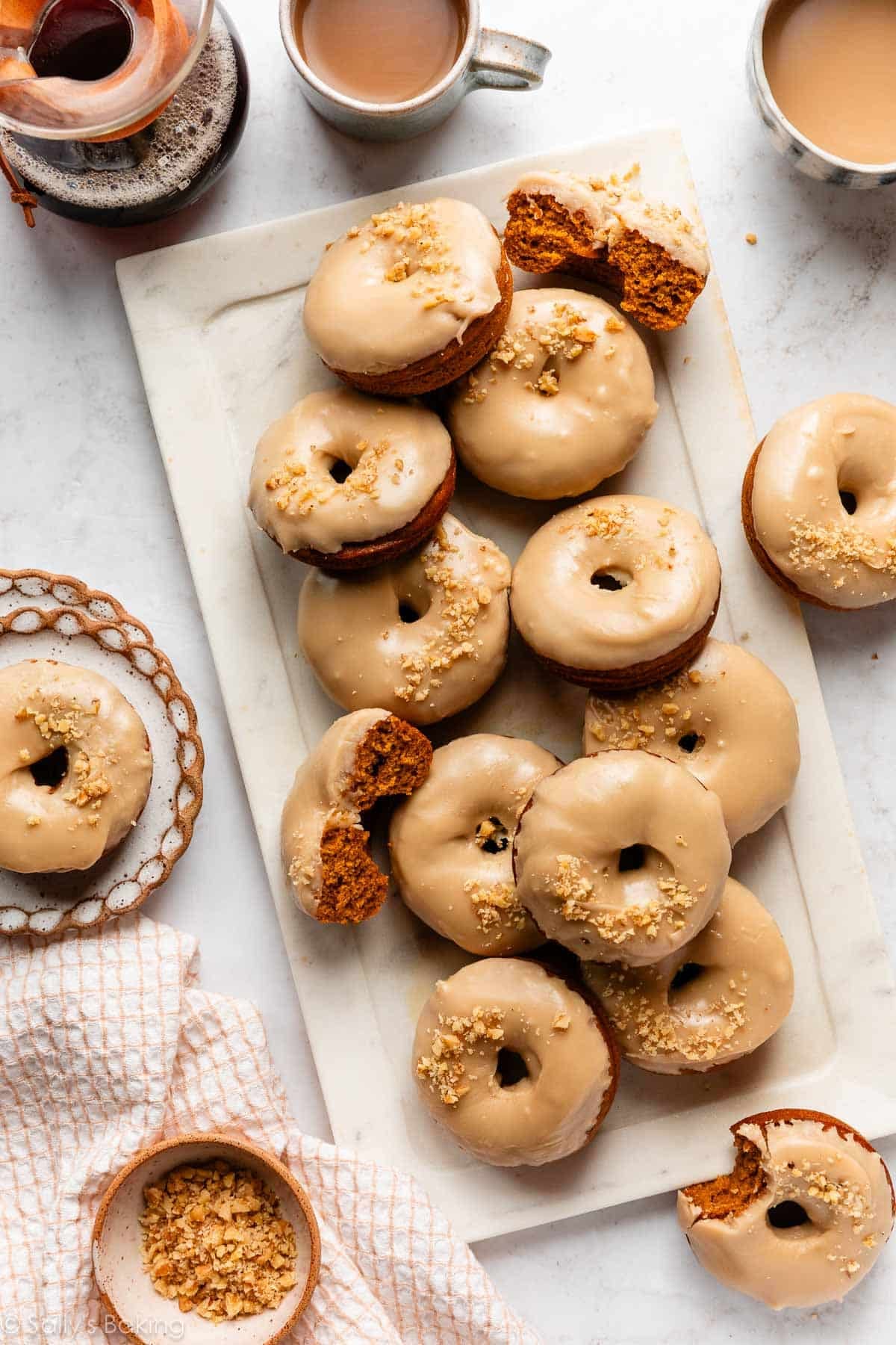 pumpkin donuts with brown sugar icing with crushed walnuts on top with mugs of coffee.