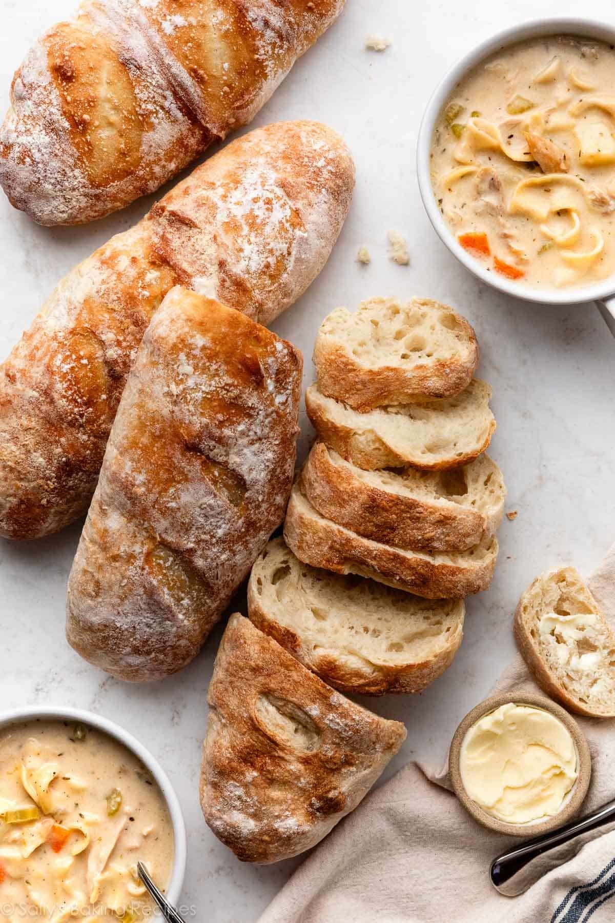 loaves of homemade artisan bread with bowls of chicken noodle soup.