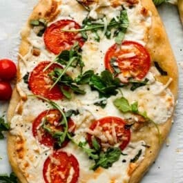 homemade flatbread pizza with mozzarella cheese, tomatoes, and arugula on top.