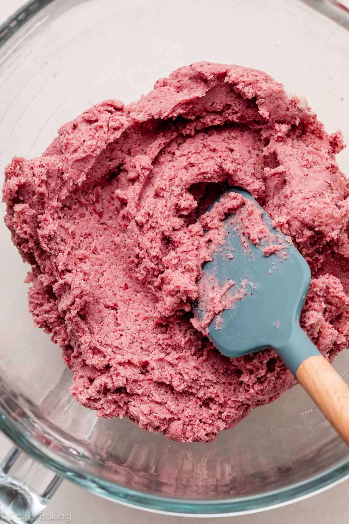 pink raspberry cookie dough with blue spatula in glass bowl.