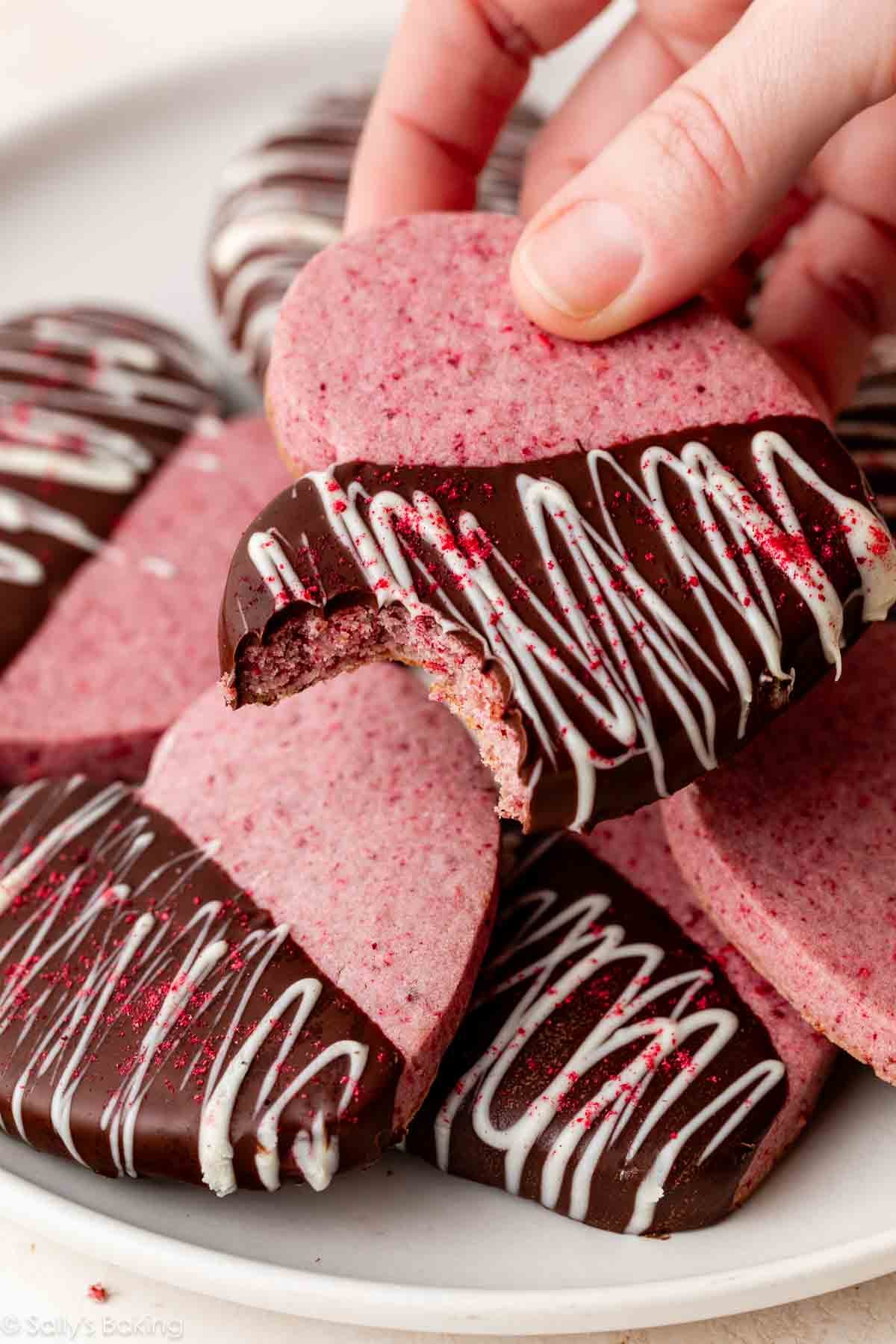 hand holding raspberry sugar cookie with bite taken out of it.