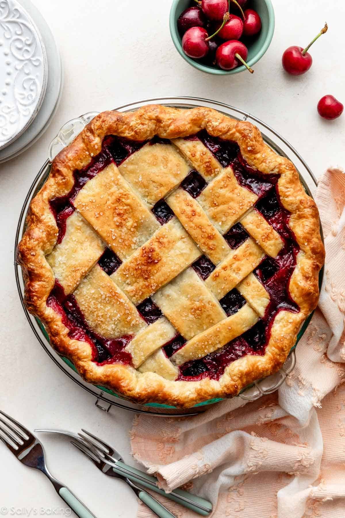 homemade cherry pie with lattice crust on top with pink linen and fresh cherries.