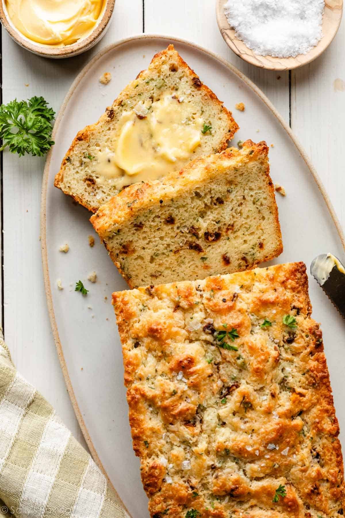 savory quick bread slices with butter, sun-dried tomatoes, parsley, and fresh basil.