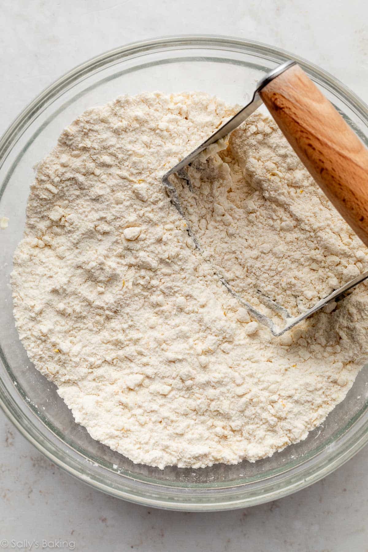 pastry cutter and dry ingredients with butter cut in in glass bowl.