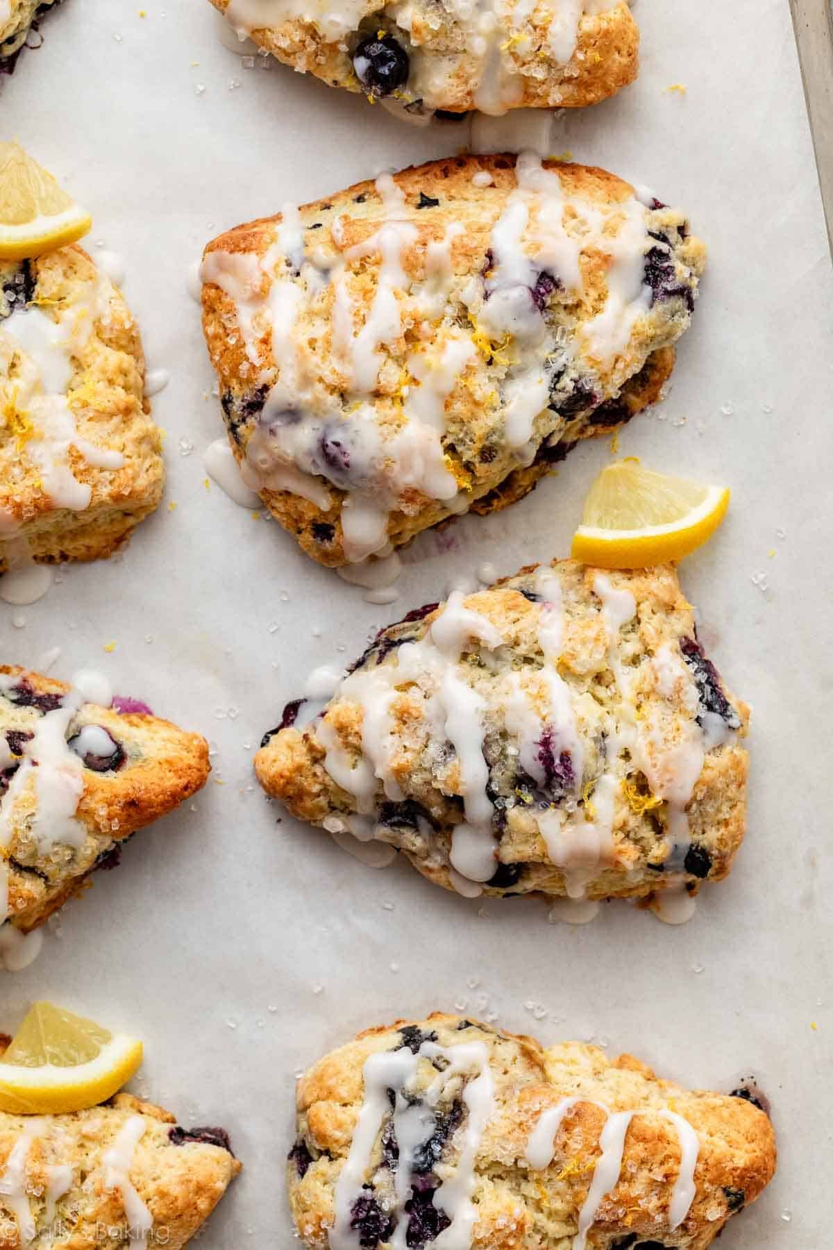 lemon blueberry scones with icing on parchment paper-lined baking sheet.