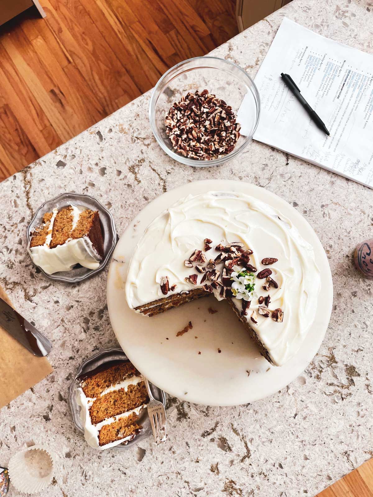 carrot cake on cake stand with slices on plates next to it.