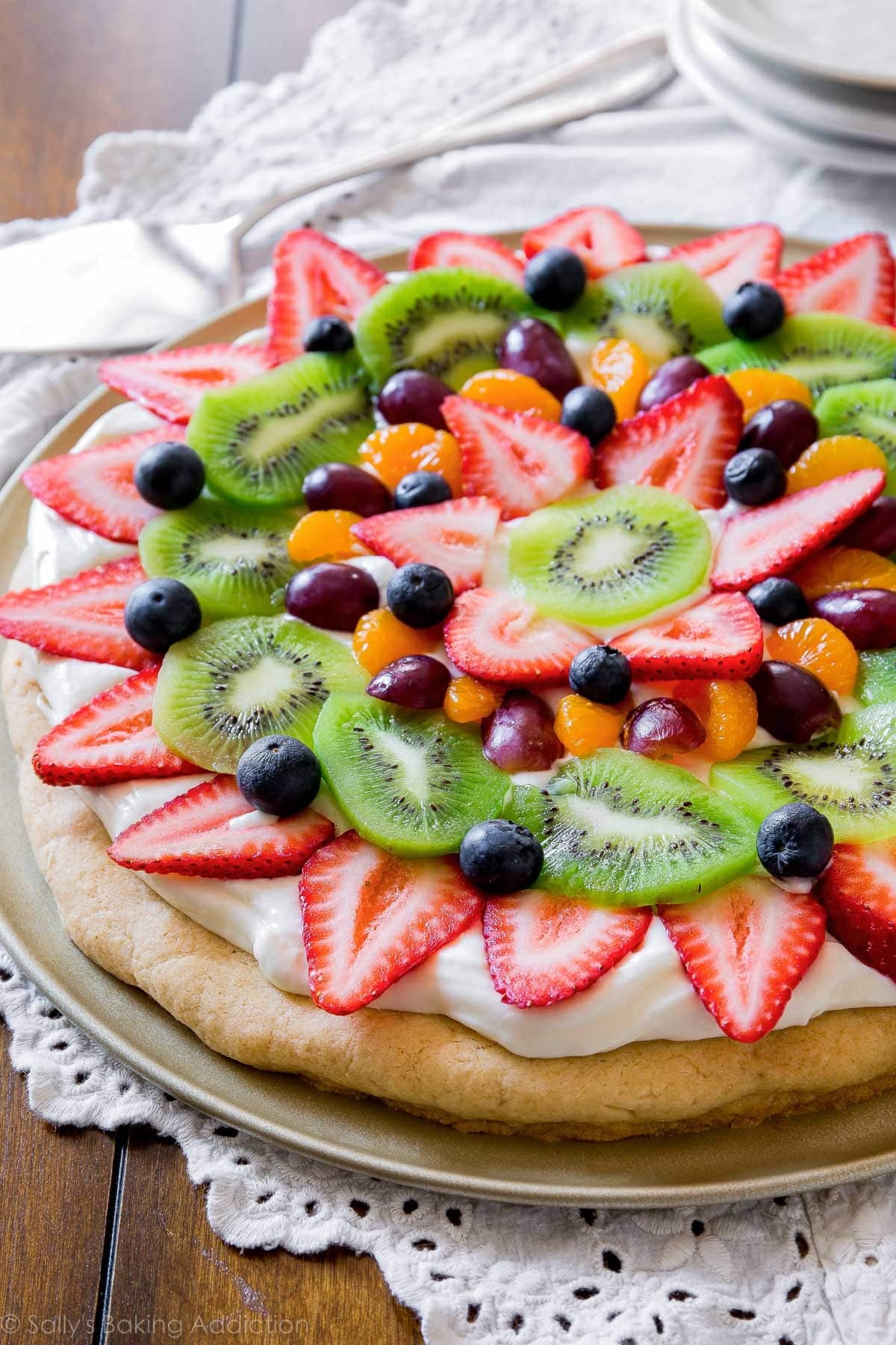 decorated sugar cookie fruit pizza on pizza pan with strawberries, kiwi, blueberries, grapes, and mandarin oranges on top.