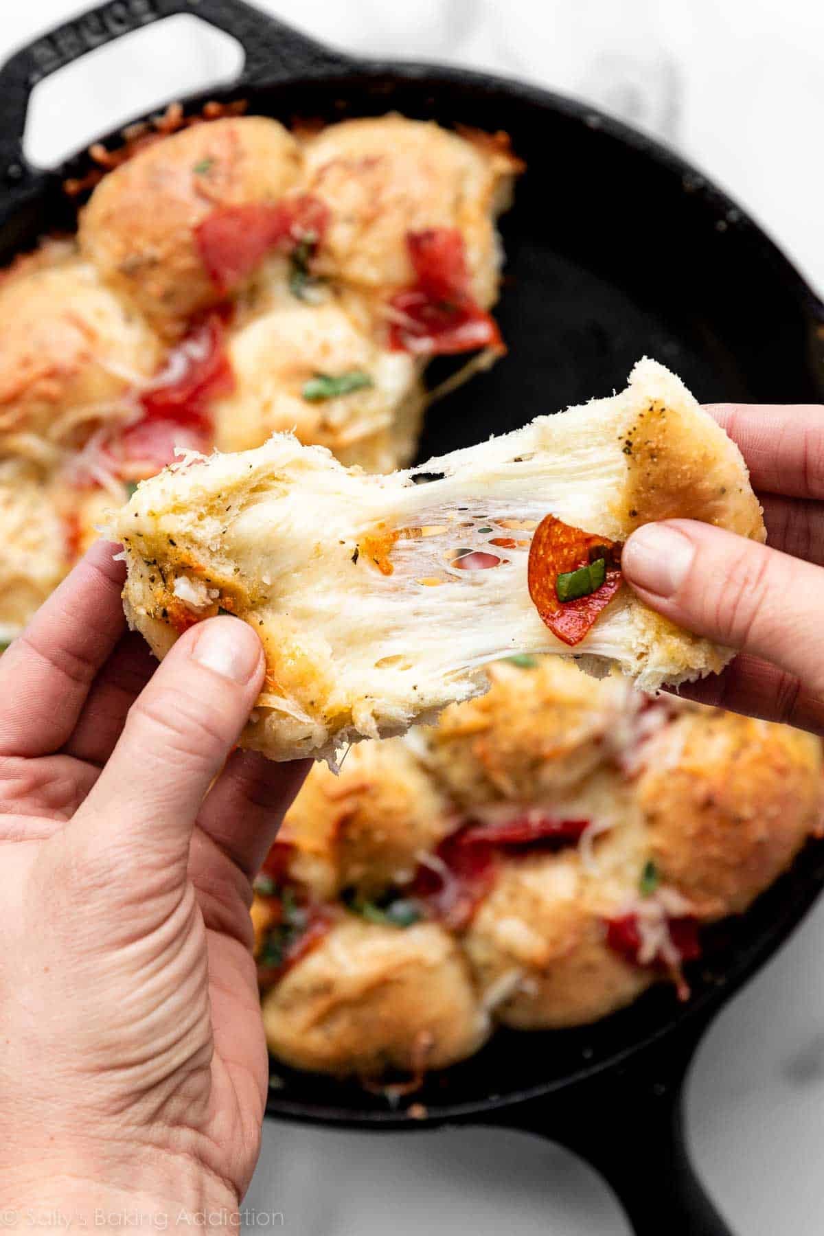 pulling apart a cheesy stuffed pizza roll to reveal cheese and pepperoni inside.