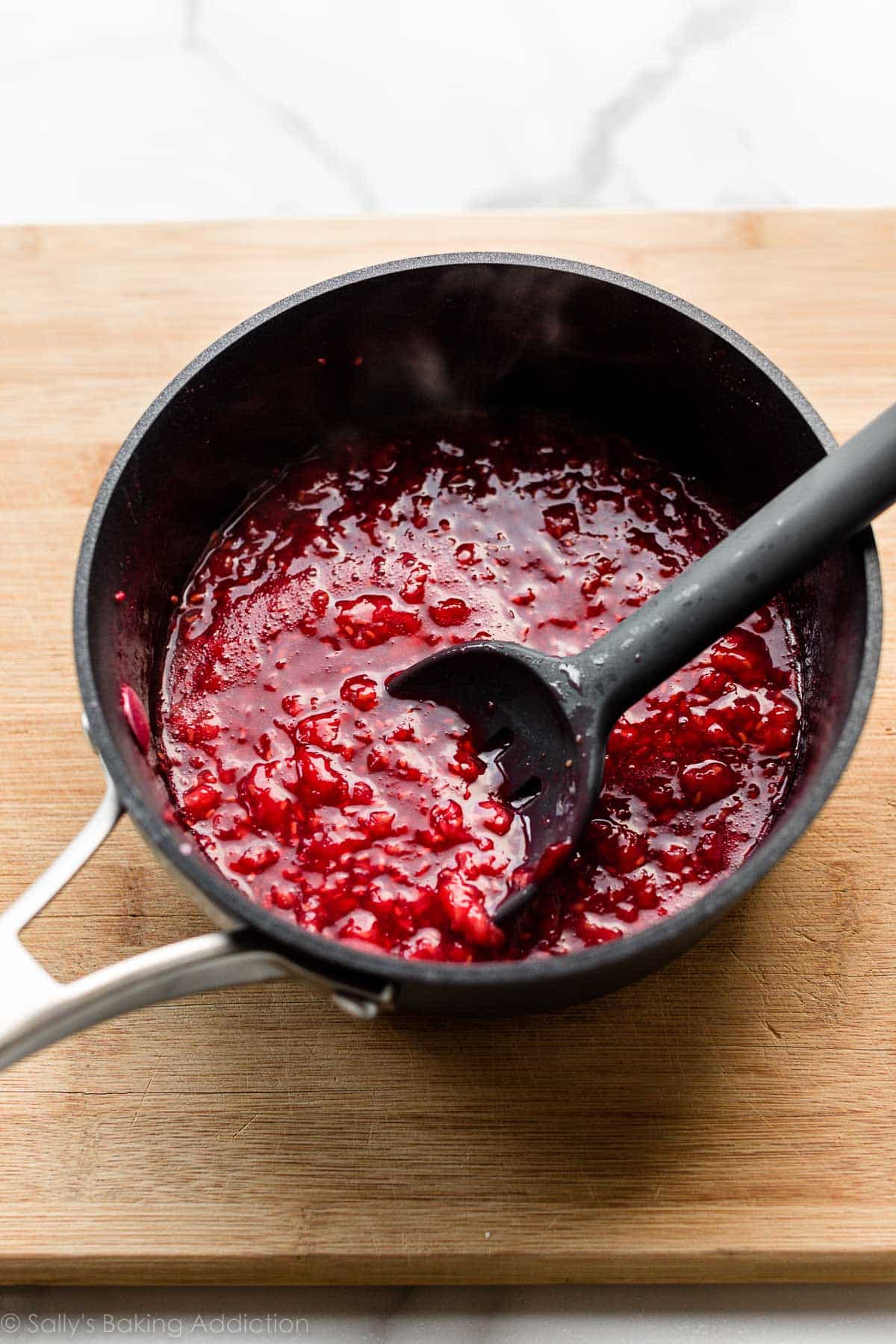 cooked raspberry dessert topping in saucepan sitting on wooden cutting board.