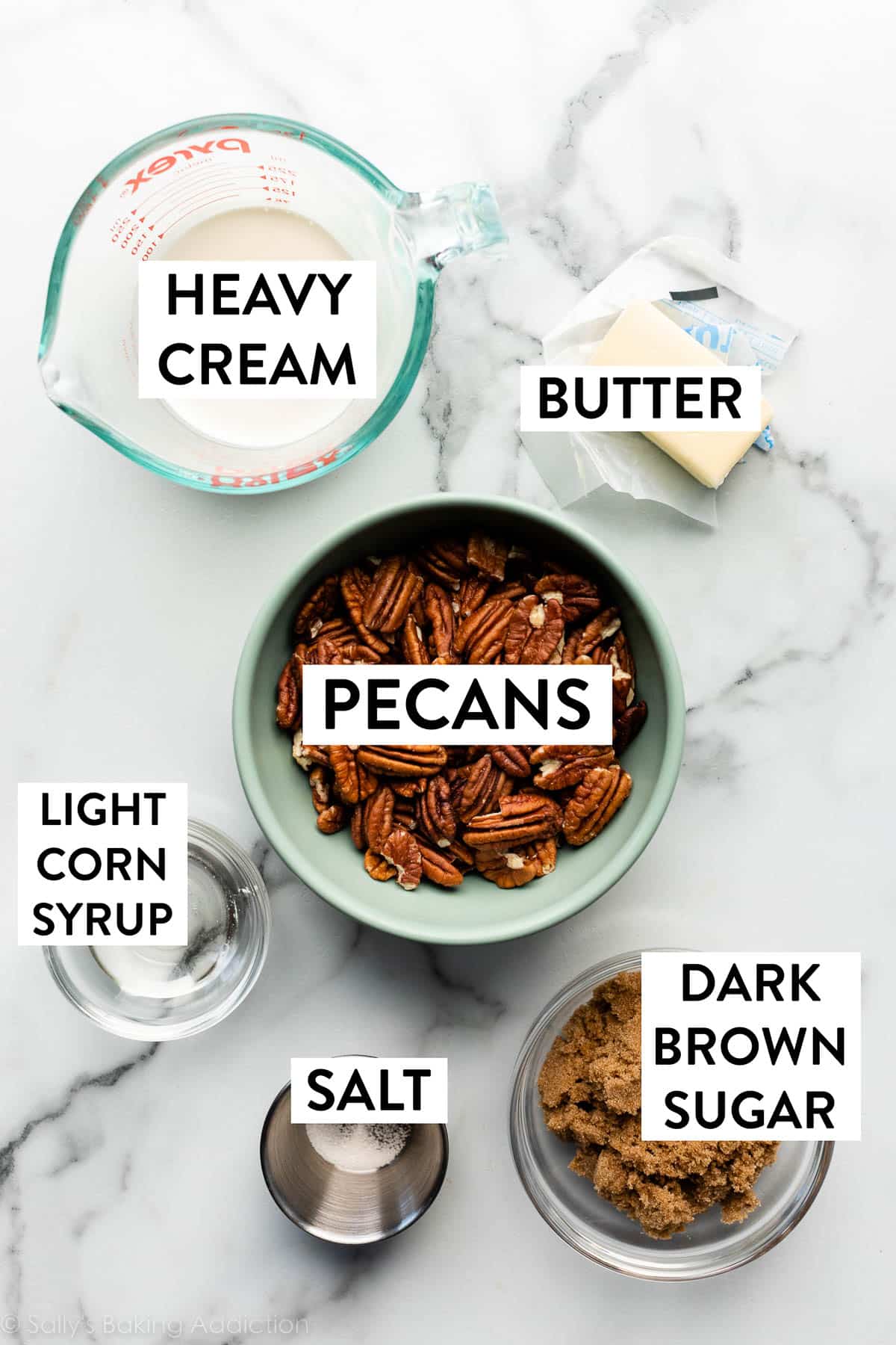 ingredients on marble countertop including pecans, heavy cream, butter, dark brown sugar, light corn syrup, and salt.