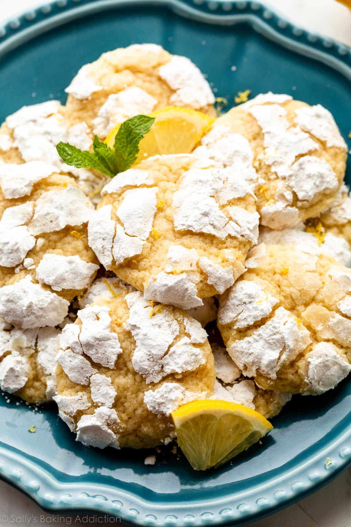 lemon crinkle cookies arranged on blue plate with lemon slices and fresh mint.