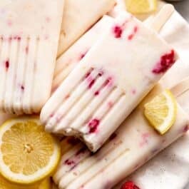 creamy lemon popsicles with raspberries inside on plate with fresh lemon slices.