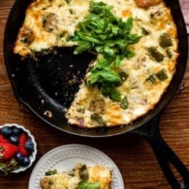 chicken sausage and green pepper frittata with fresh arugula on top in cast iron skillet.