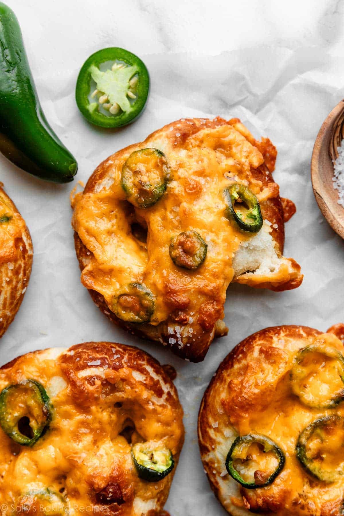 homemade soft pretzel topped with jalapeño slices and melted cheese with piece ripped off.