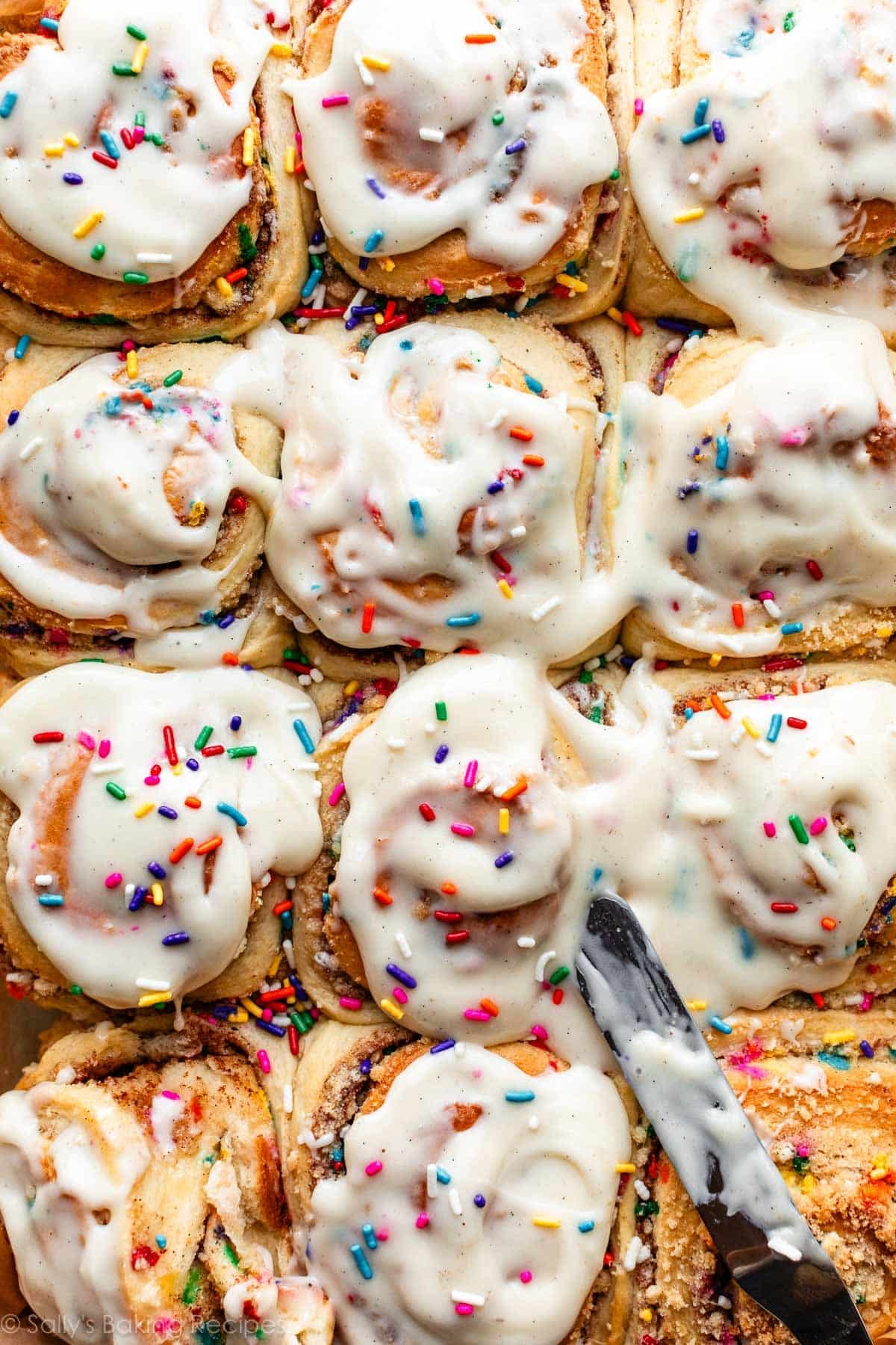 spreading cream cheese icing on sprinkle funfetti cake cinnamon rolls.