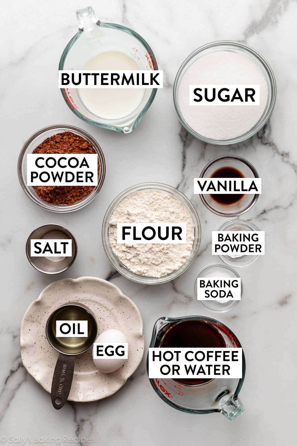 ingredients on marble counter including cocoa powder, buttermilk, flour, egg, oil, sugar, and salt.