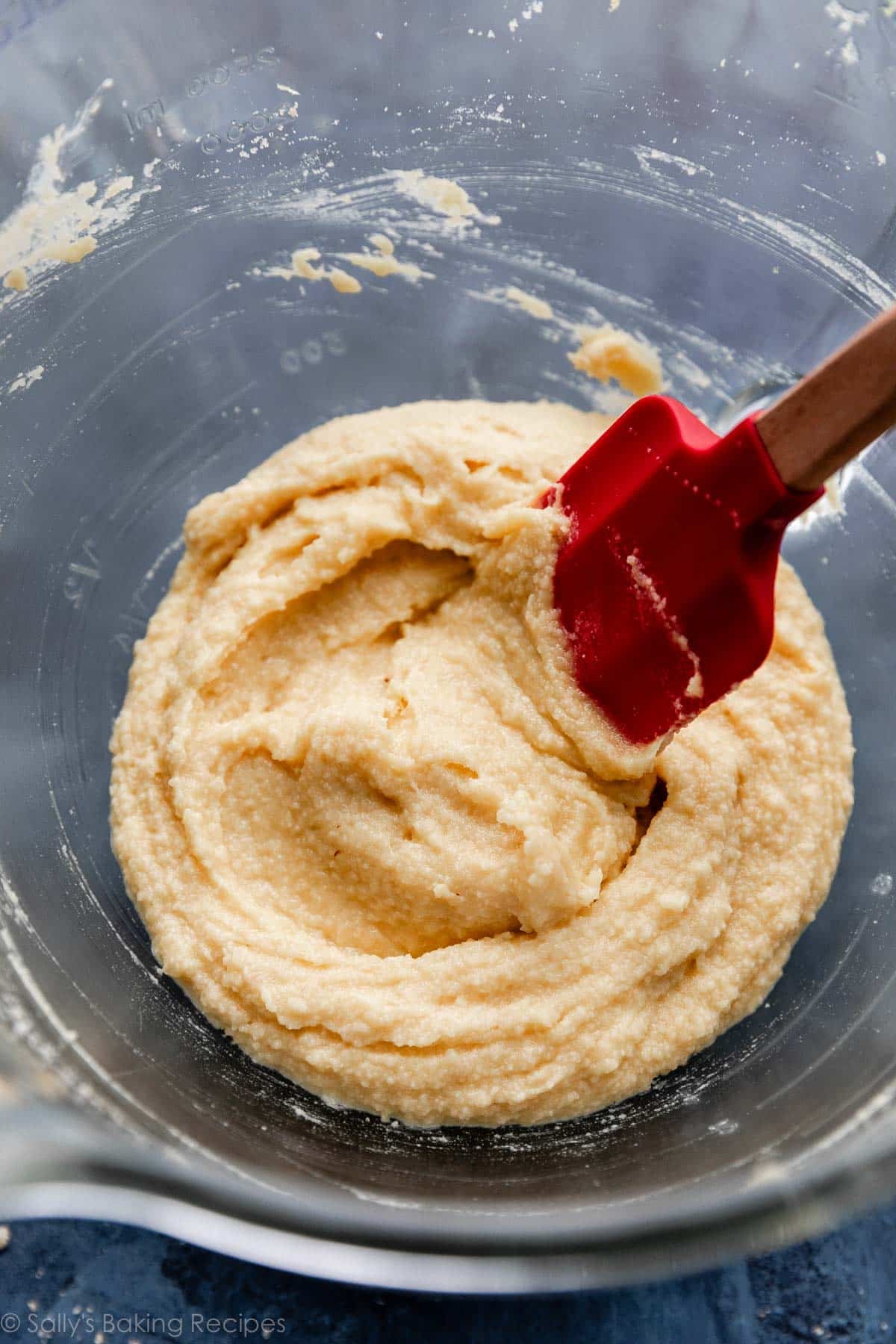 red spatula stirring almond frangipane cream in glass bowl.