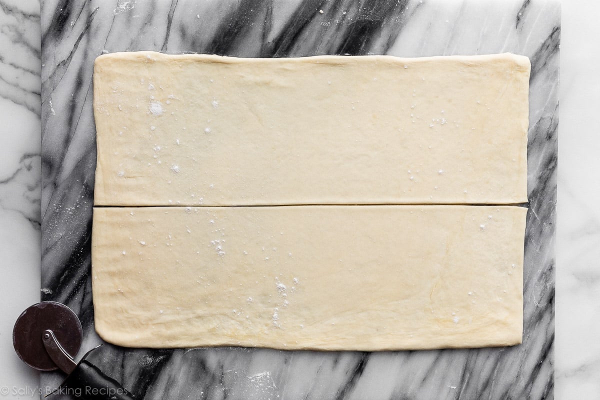 rolled out pastry dough cut in half on top of marble board.