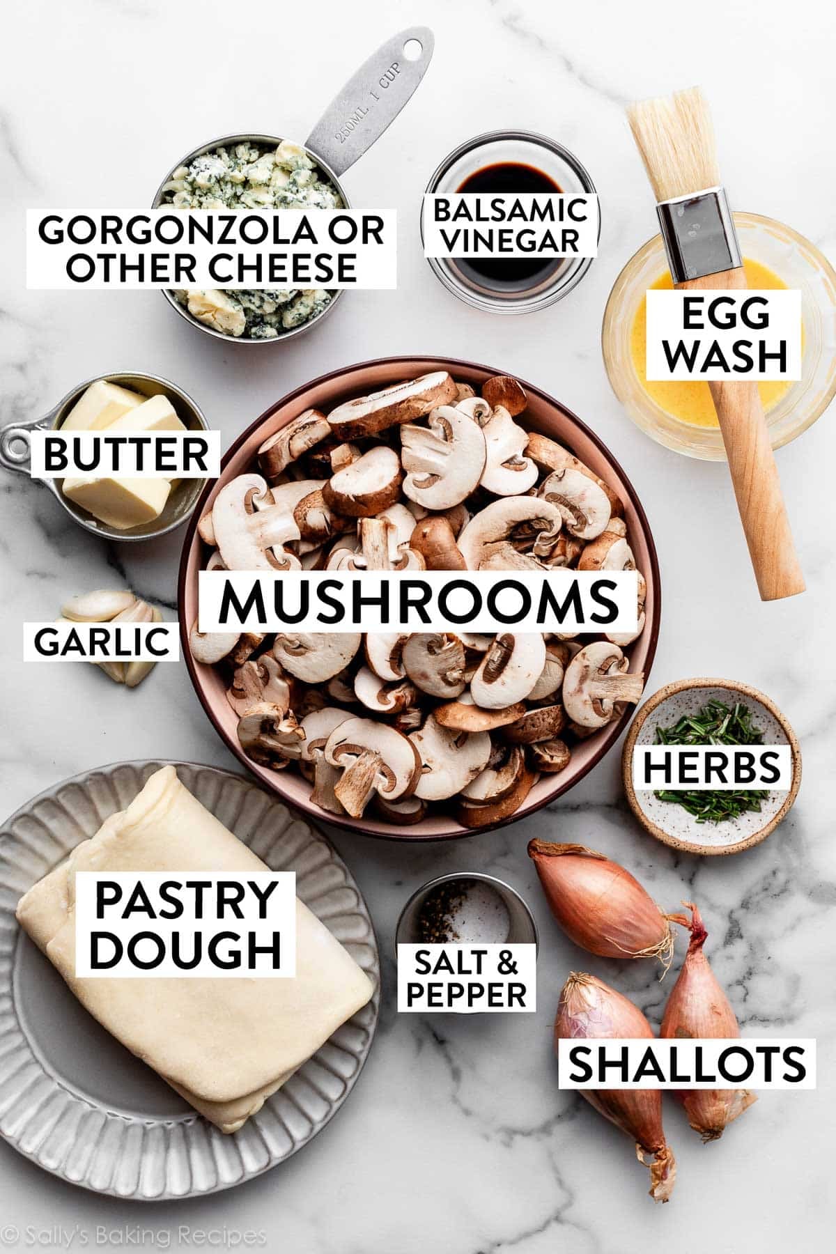 ingredients on marble counter including gorgonzola cheese, garlic ,pastry dough, shallots, herbs, and mushrooms.
