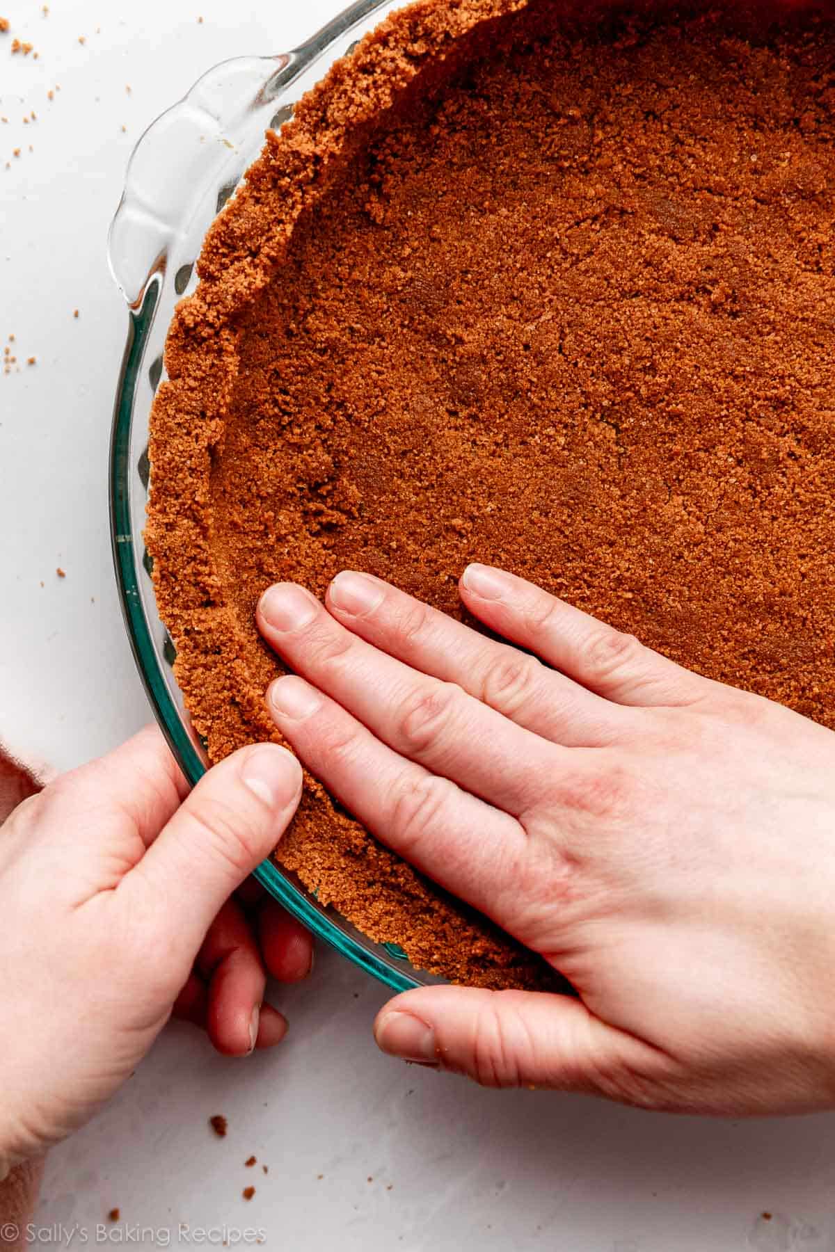 hands pressing Biscoff cookie pie crust into glass pie dish.