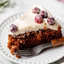 slice of gingerbread cake with cream cheese frosting on top and sugared cranberries.
