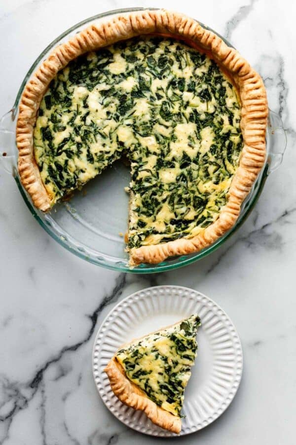 spinach quiche with slice cut out and set on plate.