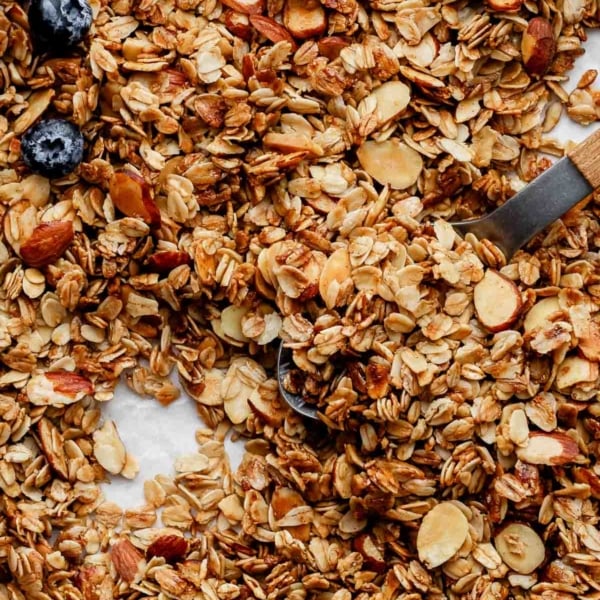 homemade vanilla almond granola spread on lined baking sheet with a couple fresh strawberries and blueberries.