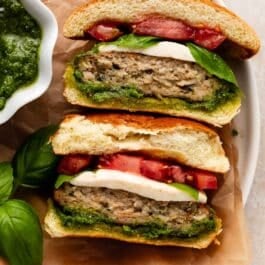 caprese pesto chicken burger with tomato and basil cut in half and face up.
