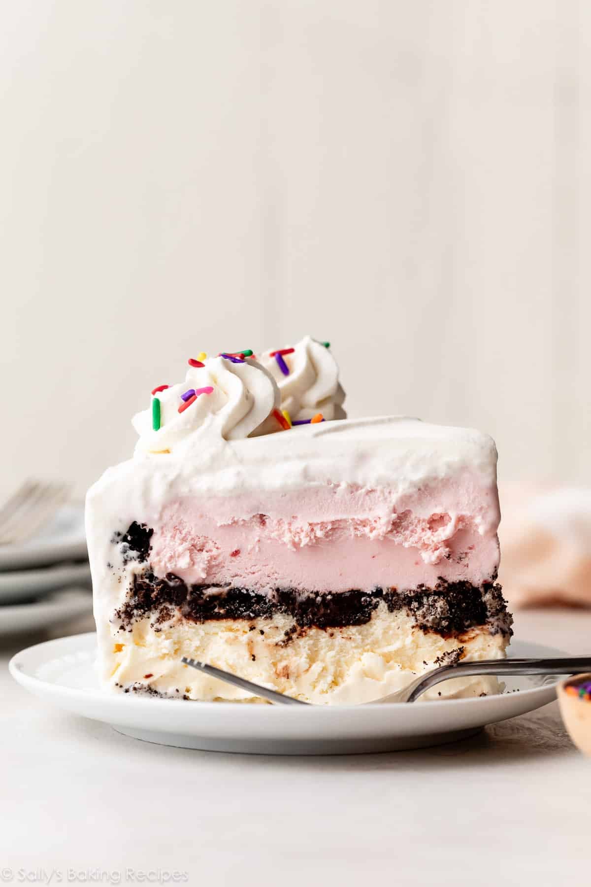 vanilla, Oreo, strawberry ice cream cake slice on white plate.