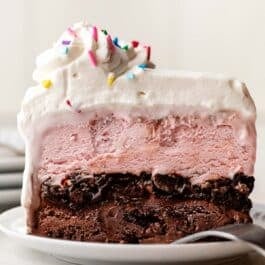 slice of ice cream cake with whipped cream and sprinkles on top on white plate.