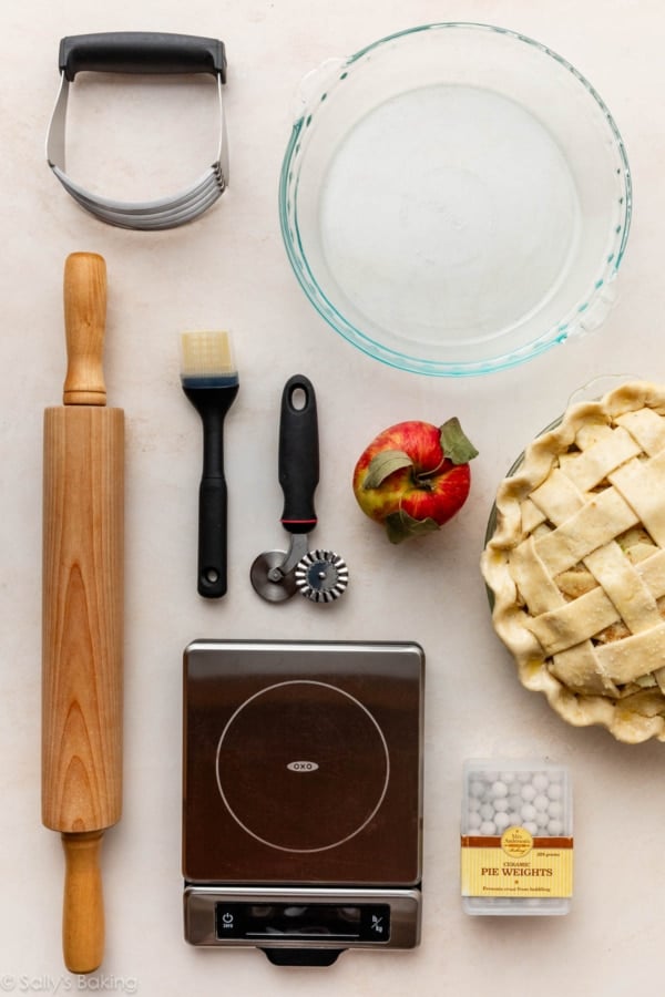 photo with a pie, pie weights, apple, pastry brush, pastry cutter, rolling pin, and food scale.