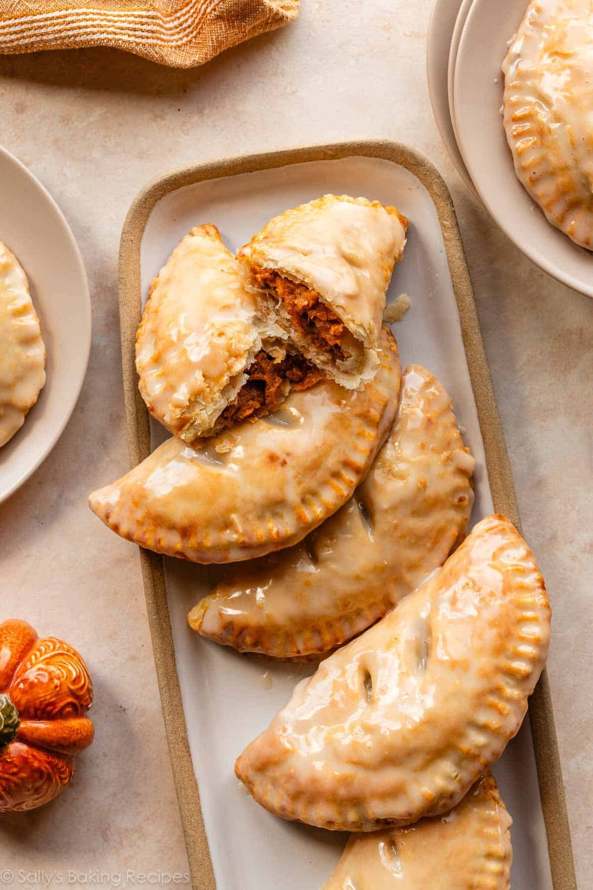 glazed pumpkin hand pies with one cut in half on serving tray on beige surface.