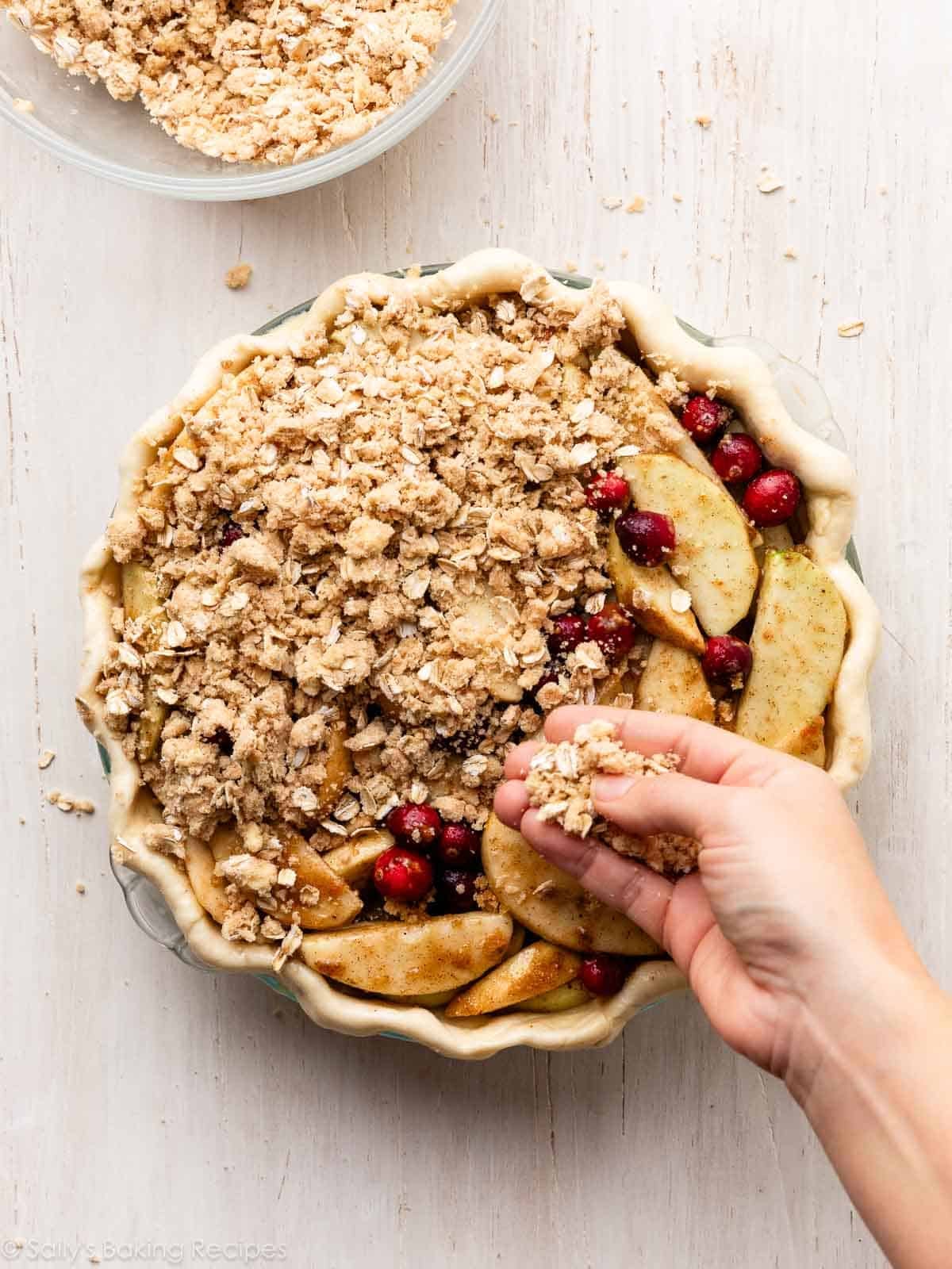 hand sprinkling oat crumble topping on pie filling.
