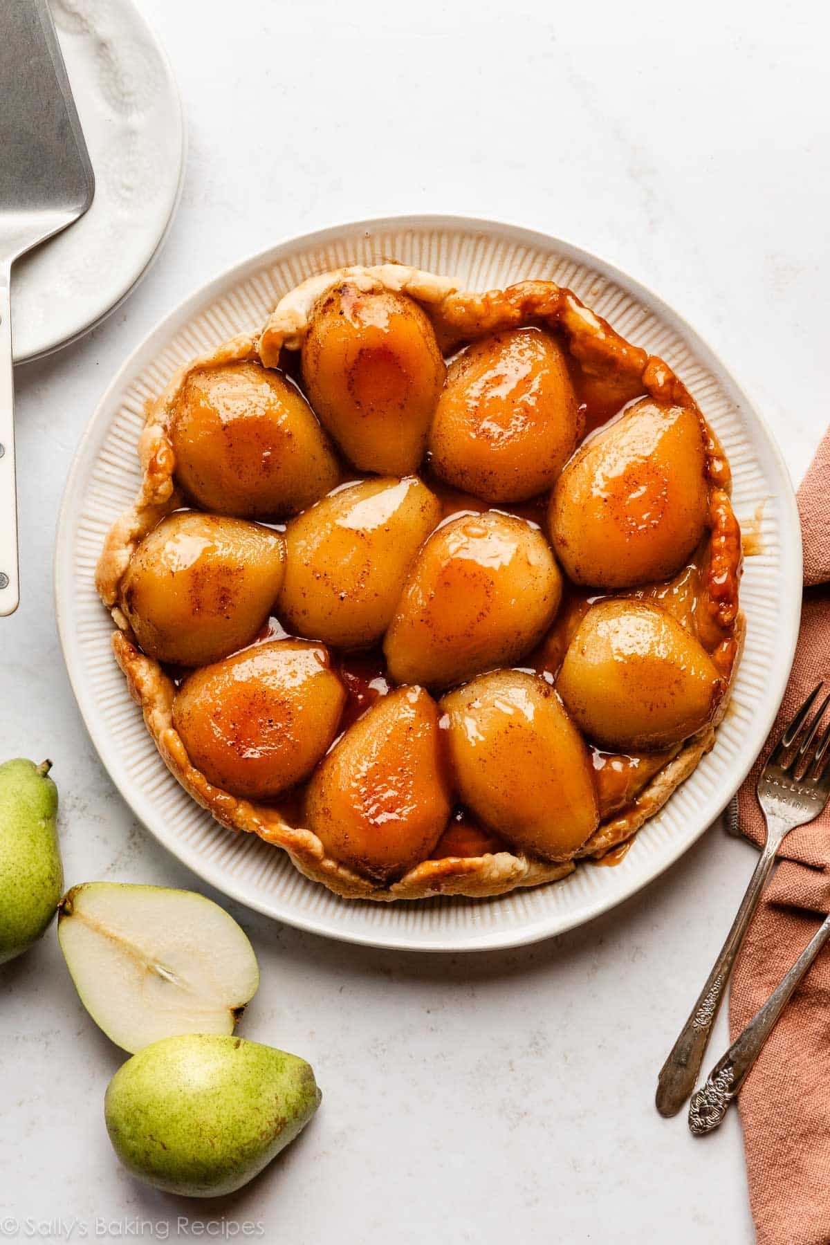 pear tarte tatin on white serving plate with fresh pears on the side.