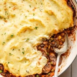 spoon in dish of vegetarian shepherd's pie with mashed potato topping.