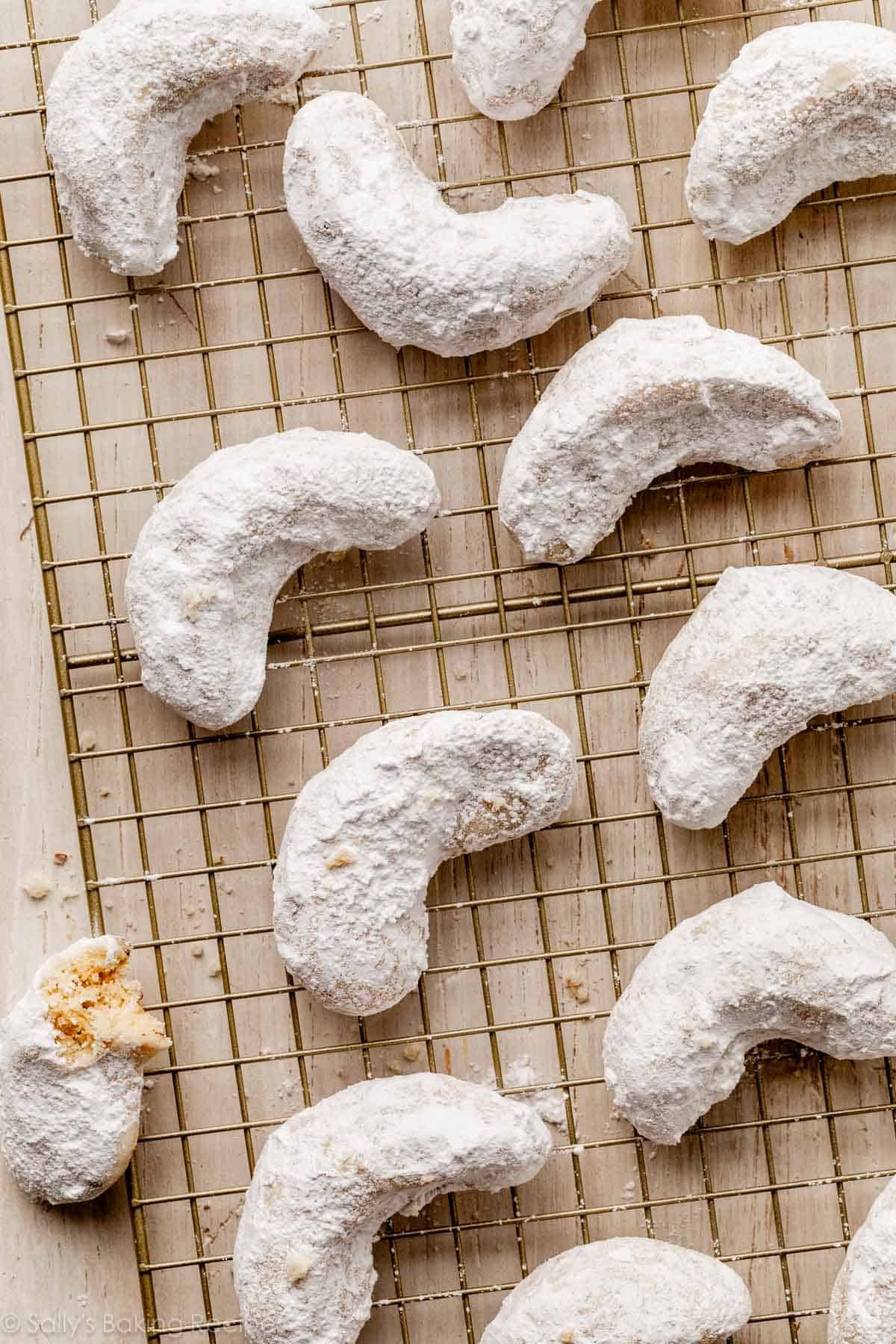 almond crescent-shaped cookies coated in powdered sugar on gold wire cooling rack.