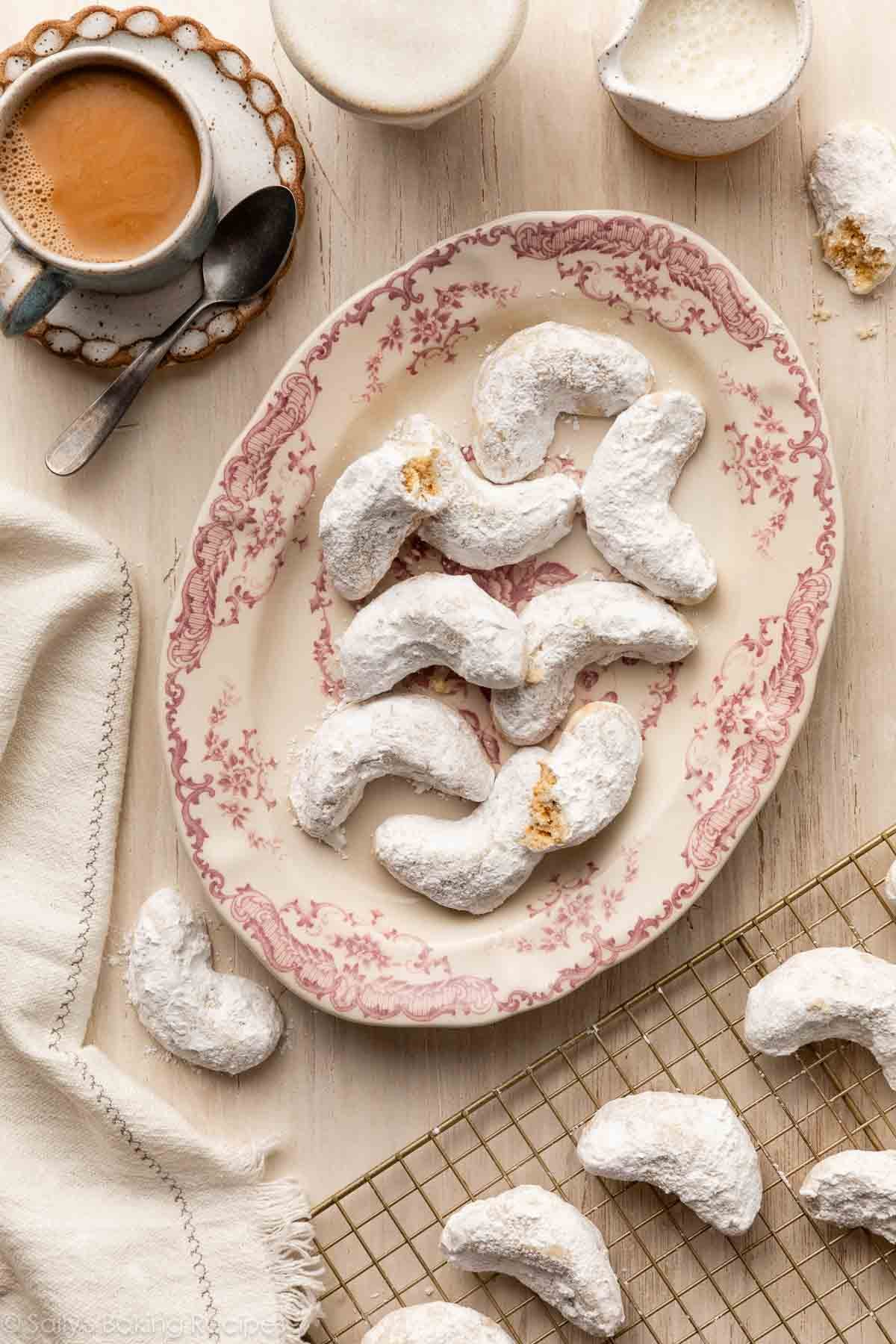 almond crescent cookies on pink floral plate with white linen and coffee next to it.
