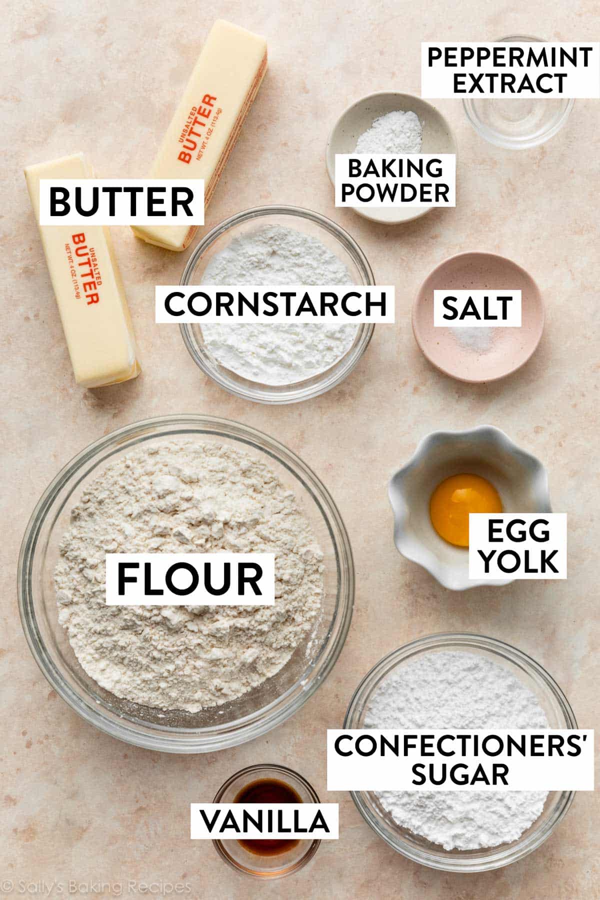 ingredients on peach surface including flour, butter, egg yolk, confectioners' sugar, vanilla, and cornstarch.