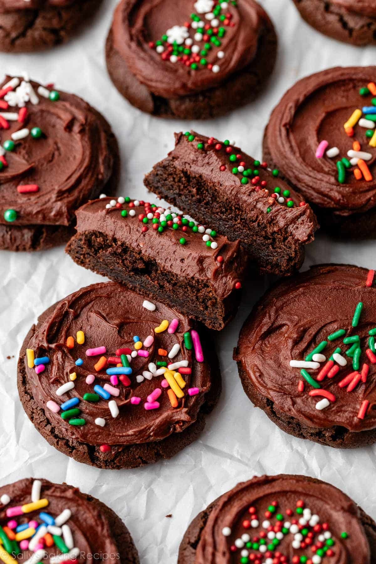 chocolate frosted cookies with rainbow and Christmas sprinkles with one cut in half to show fudge-like center.