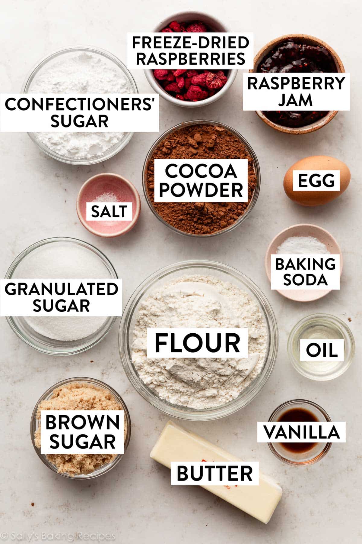 ingredients measured on counter in bowls including raspberry jam, cocoa powder, flour, butter, brown sugar, baking soda, oil, and salt.