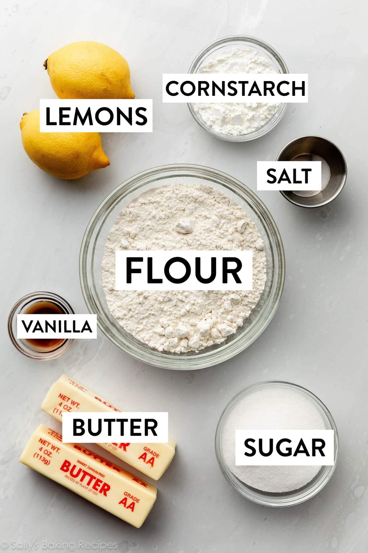 ingredients on marble surface including butter, flour, vanilla, sugar, and cornstarch.