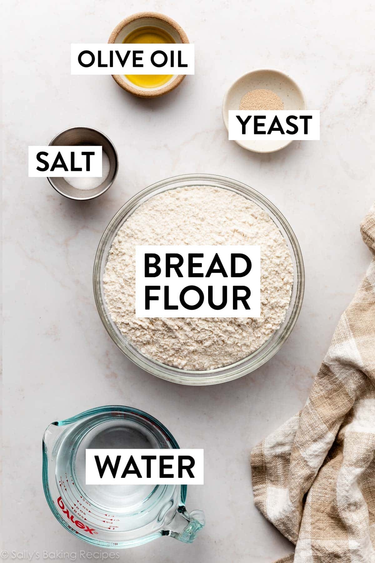 ingredients on marble surface including bread flour, water, yeast, olive oil, and salt.