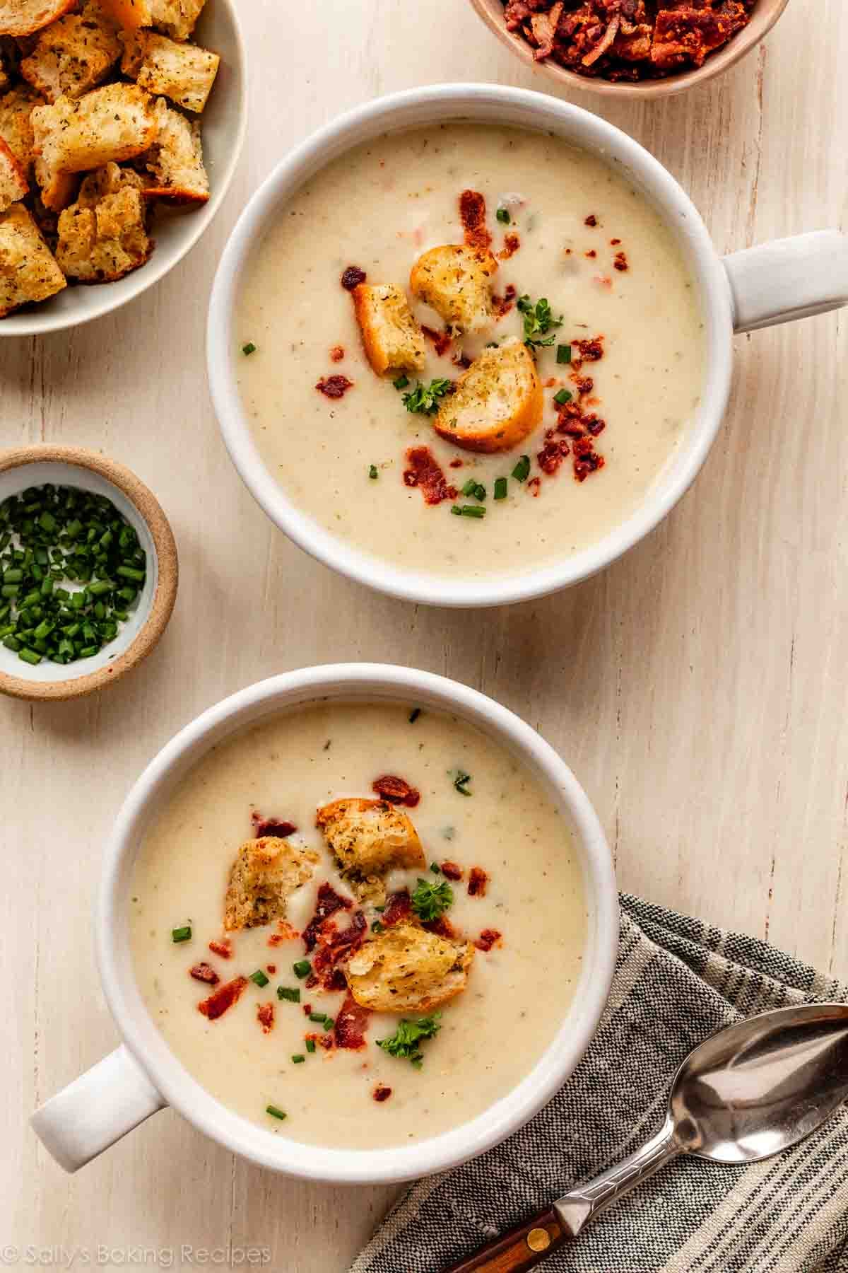 2 bowls of cauliflower potato soup with croutons, bacon, and chopped chives on top.